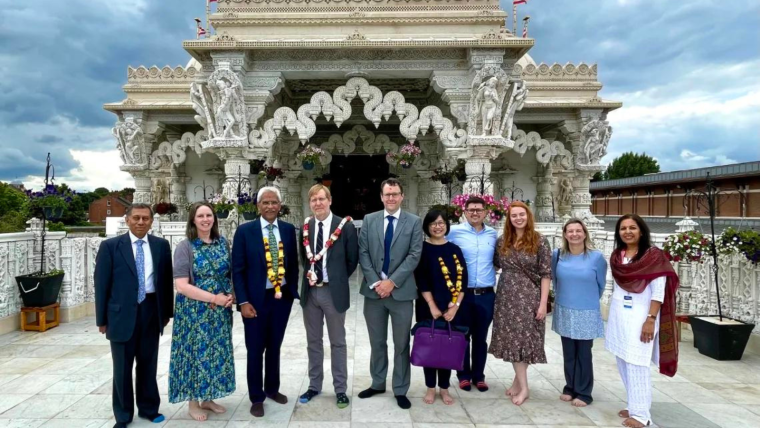 A cluster of people in fine clothes and garlands stand in front of the Neasden Temple