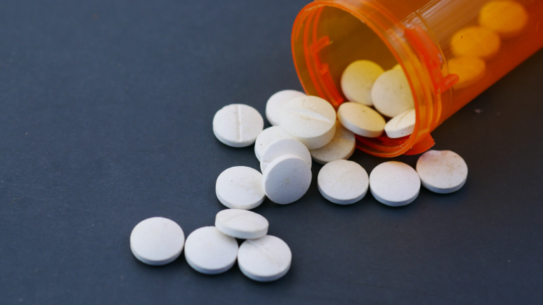 Generic pill bottle with white circular pills spilling out against a dark background