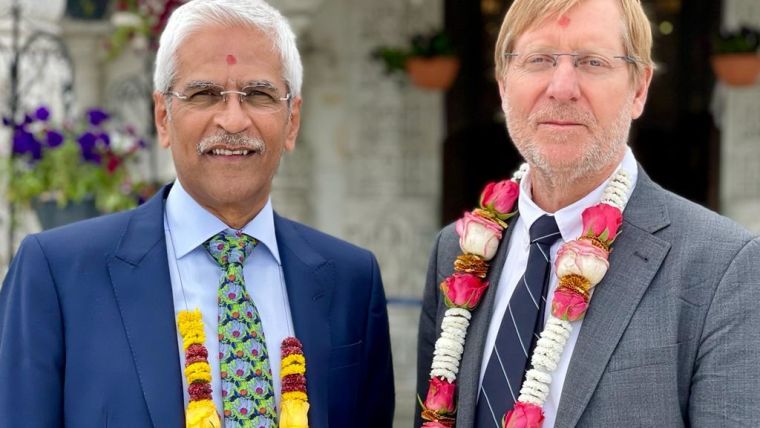Professor Mahendra Patel and Professor Chris Butler at the BAPS UK & Europe Temple. Both men are wearing garlands and are smiling at the camera.